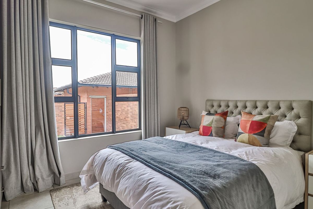 A well-maintained bedroom featuring large aluminium-framed windows, built-in cupboards, and neutral wall finishes, offering a bright and comfortable living space.