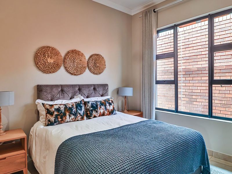 A well-maintained bedroom featuring neutral wall tones, large windows with dark frames, and tiled flooring.