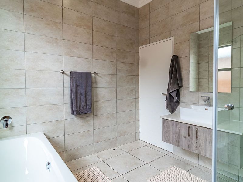 Modern bathroom featuring a wall-mounted vanity, a glass-enclosed shower, and a separate bathtub with neutral floor-to-ceiling tiling.