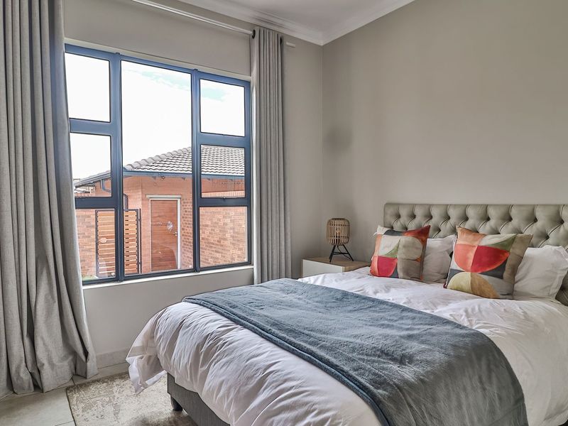A well-maintained bedroom featuring large aluminium-framed windows, built-in cupboards, and neutral wall finishes, offering a bright and comfortable living space.