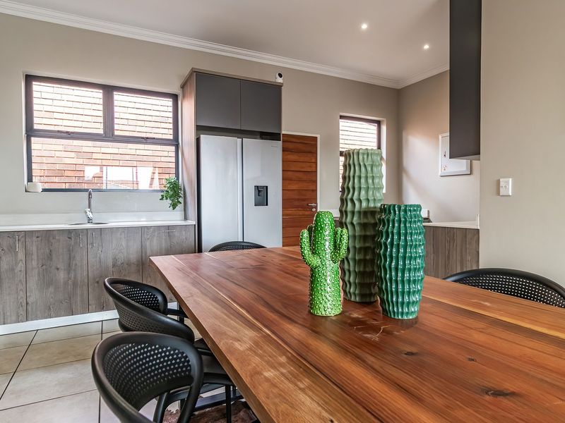 Modern open-plan kitchen and dining area featuring wood-grain cabinetry, stone countertops, recessed lighting, and tiled flooring.