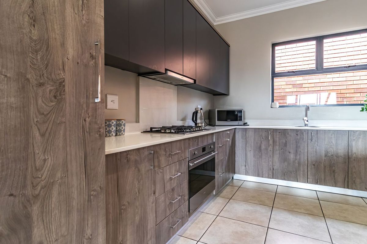 Modern kitchen featuring wood-grain cabinetry, stone countertops, built-in oven, gas hob, extractor fan, and tiled flooring.