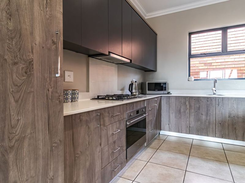 Modern kitchen featuring wood-grain cabinetry, stone countertops, built-in oven, gas hob, extractor fan, and tiled flooring.