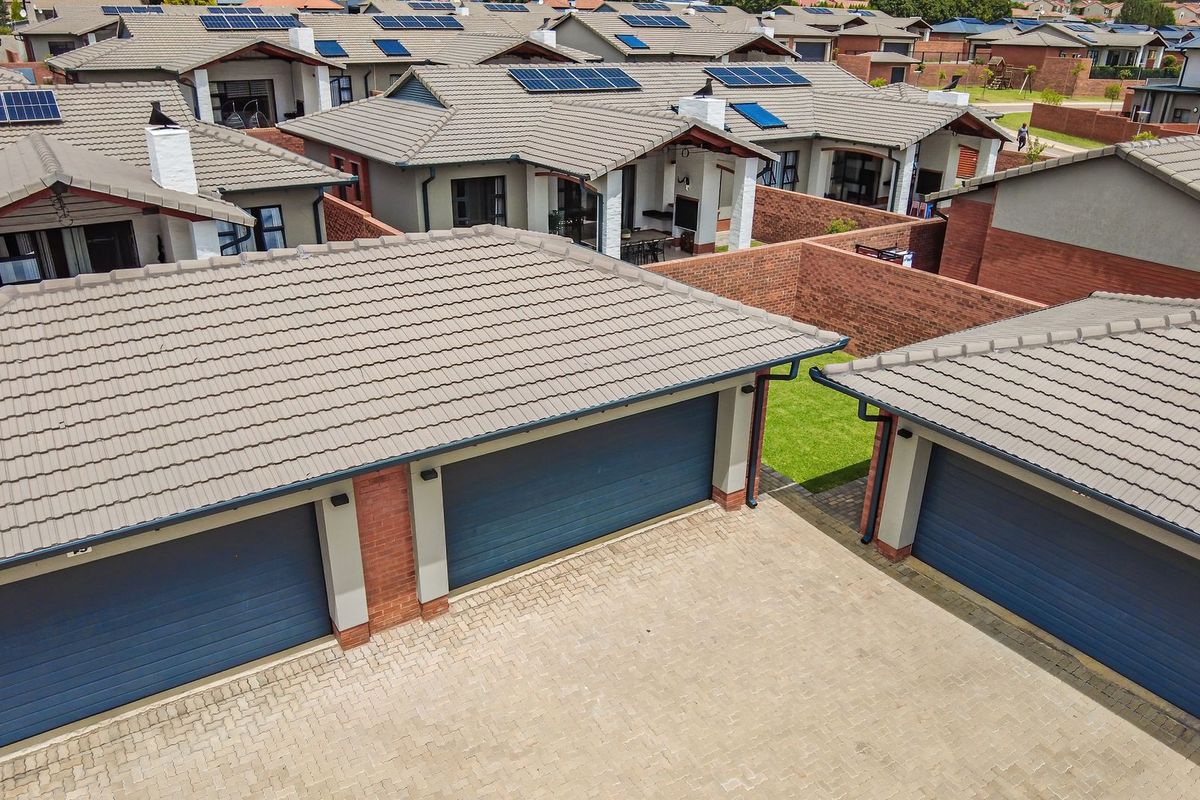 Aerial view of a townhouse complex featuring tiled roofs, solar panels, brick boundary walls, and paved driveway access to multiple garages.