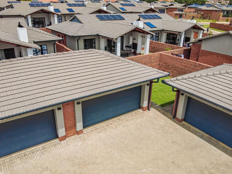 Aerial view of a townhouse complex featuring tiled roofs, solar panels, brick boundary walls, and paved driveway access to multiple garages.