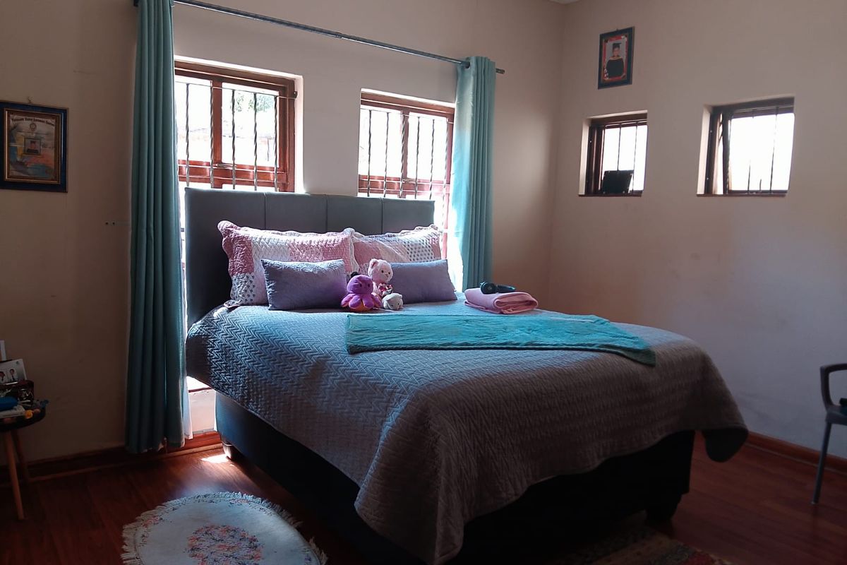 A bedroom featuring wood-look flooring, multiple windows with security bars, and neutral wall tones, providing a functional and well-lit sleeping space.