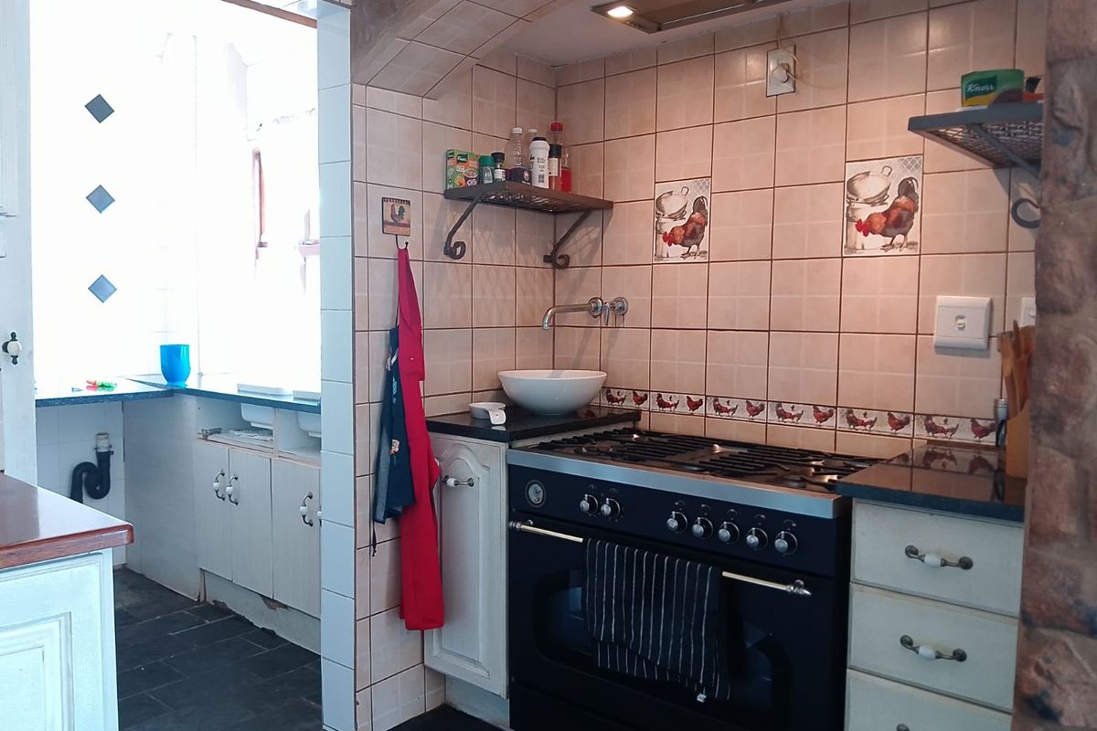A functional kitchen featuring a black freestanding gas stove, tiled splashbacks, and a secondary prep area visible through the doorway.