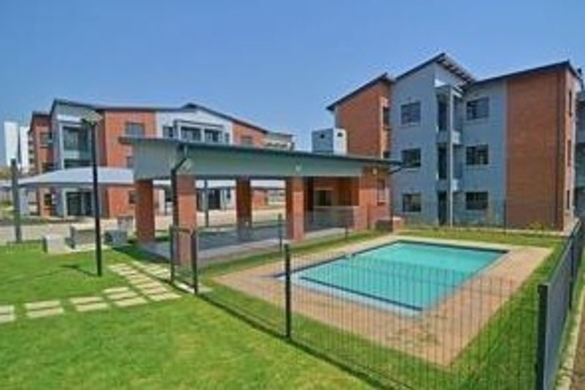 Communal outdoor area featuring a swimming pool, covered patio space, and landscaped lawn within a townhouse complex.