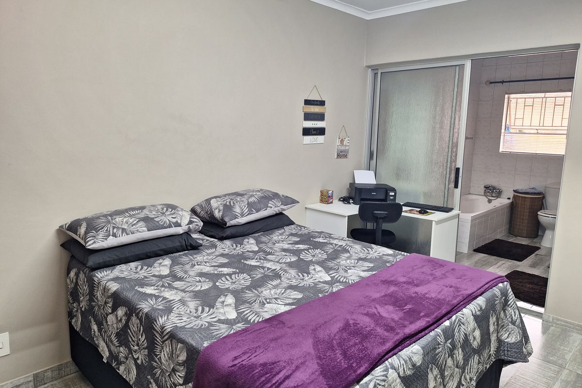 A bedroom featuring tiled flooring and an en-suite bathroom accessible through a sliding glass door, including a built-in bathtub and toilet.