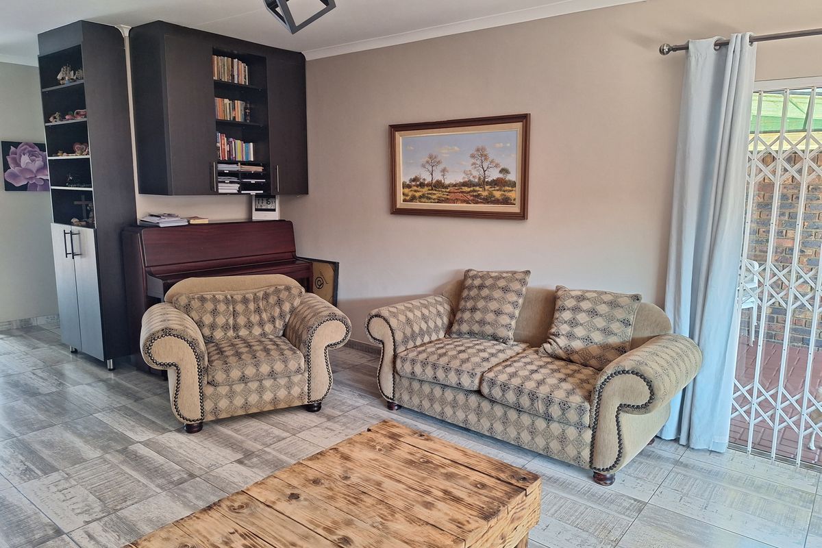 A living room featuring tiled flooring, built-in dark cabinetry with shelving, and a sliding door providing access to an outdoor patio area.