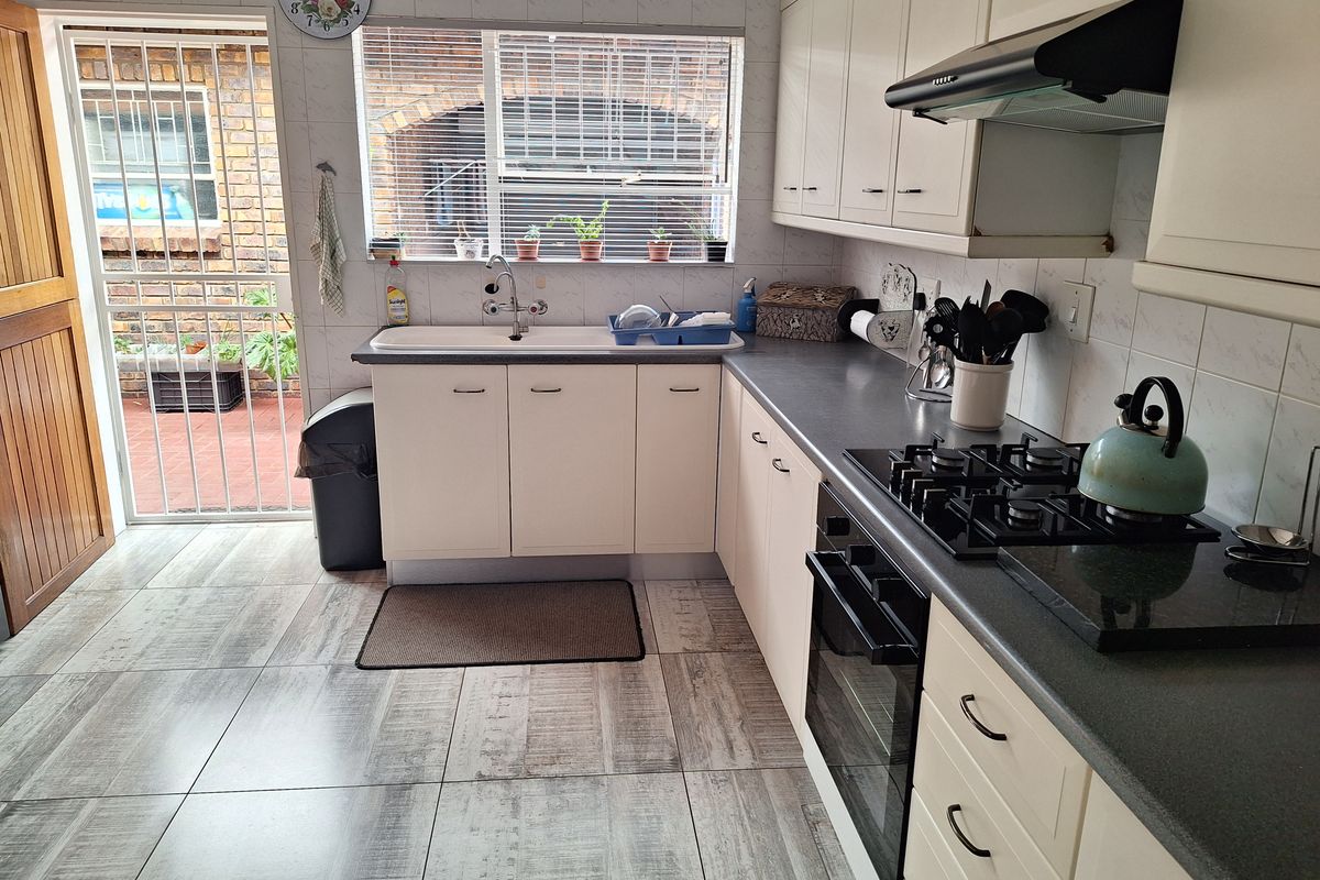 Functional kitchen featuring light-toned cabinetry, dark countertops, built-in gas hob, oven, extractor fan, and direct access to an exterior security gate.
