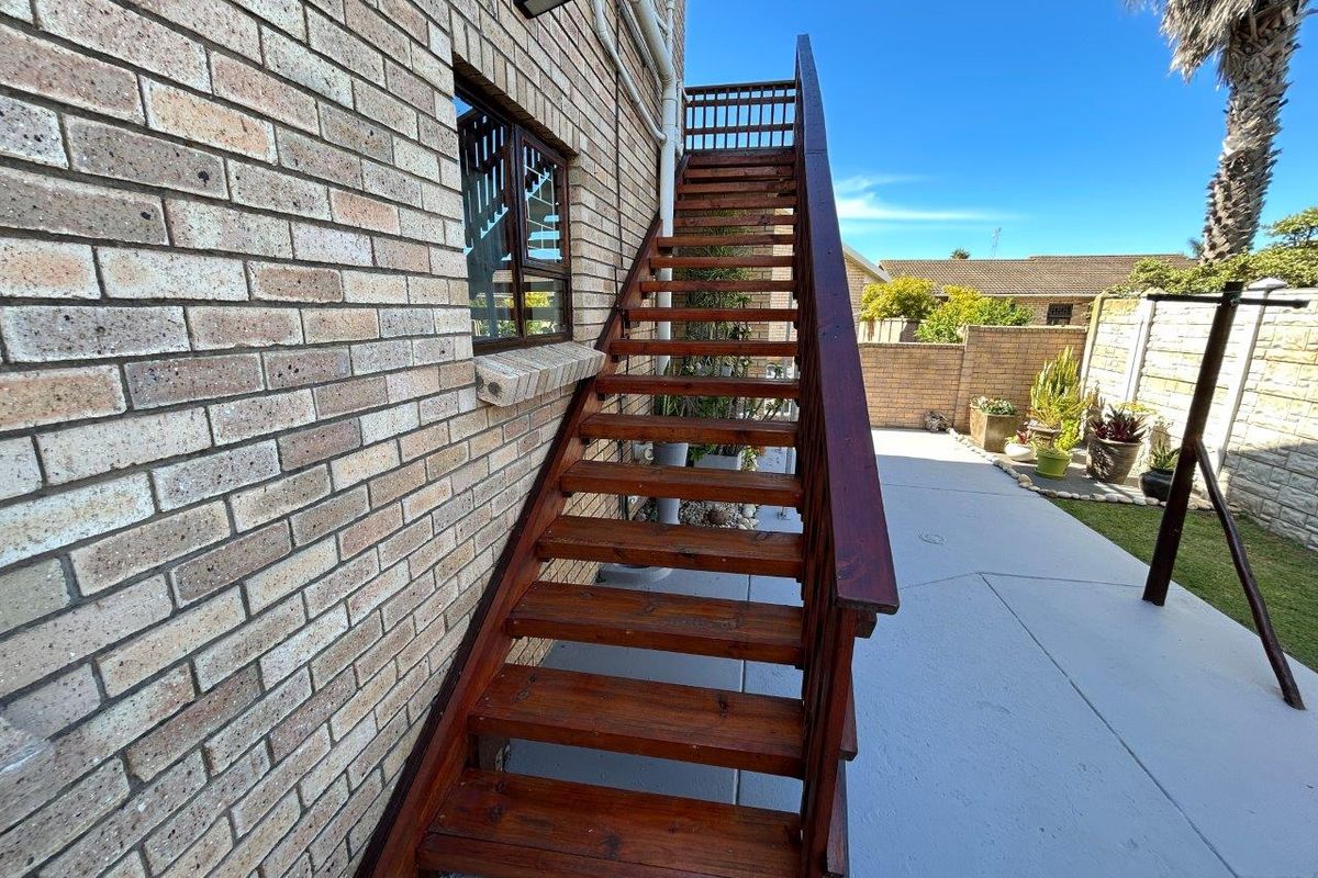 Exterior view of the property featuring a brick facade and a wooden staircase leading to an upper level, set against a paved backyard area.