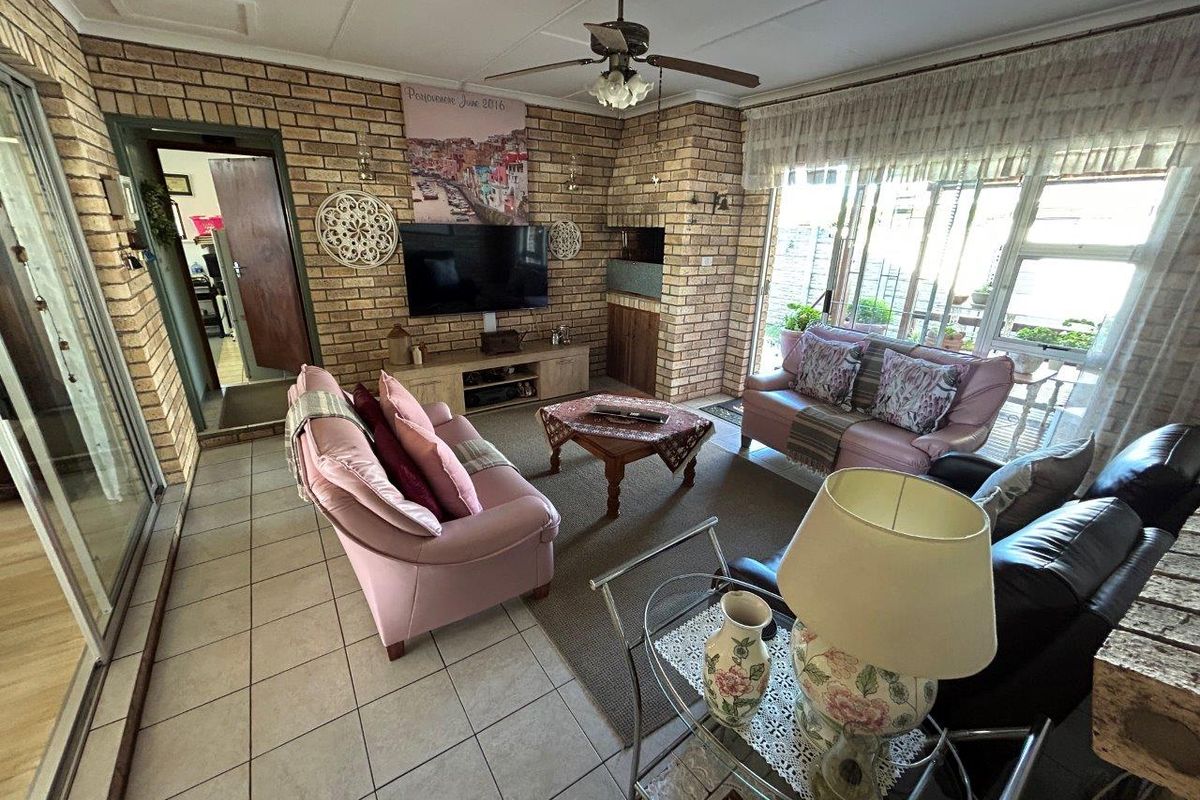 Spacious living room featuring exposed brick walls, a built-in fireplace, ceiling fan, and large windows providing natural light.
