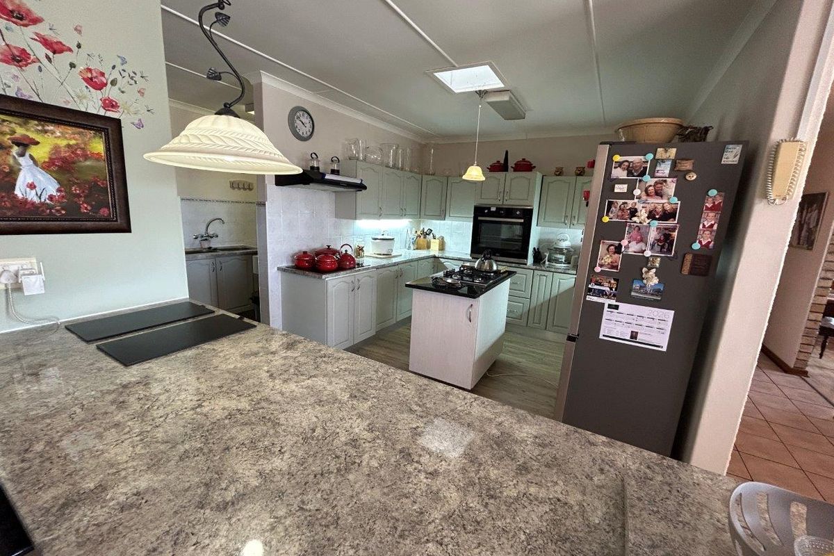 Functional kitchen featuring stone-look countertops, built-in oven, hob, and an island, with an adjacent scullery area for additional preparation and storage.