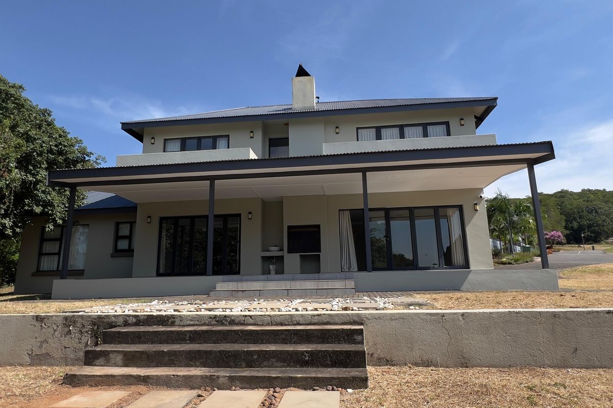Rear elevation of a two-story house featuring a covered patio with a built-in braai, sliding glass doors, and concrete stairs leading to the garden.