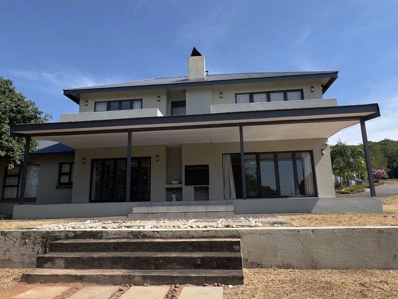 Rear elevation of a two-story house featuring a covered patio with a built-in braai, sliding glass doors, and concrete stairs leading to the garden.