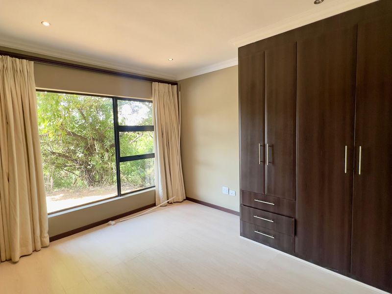 A bright and spacious bedroom featuring built-in dark wood cupboards, modern laminate flooring, and large windows with natural light.