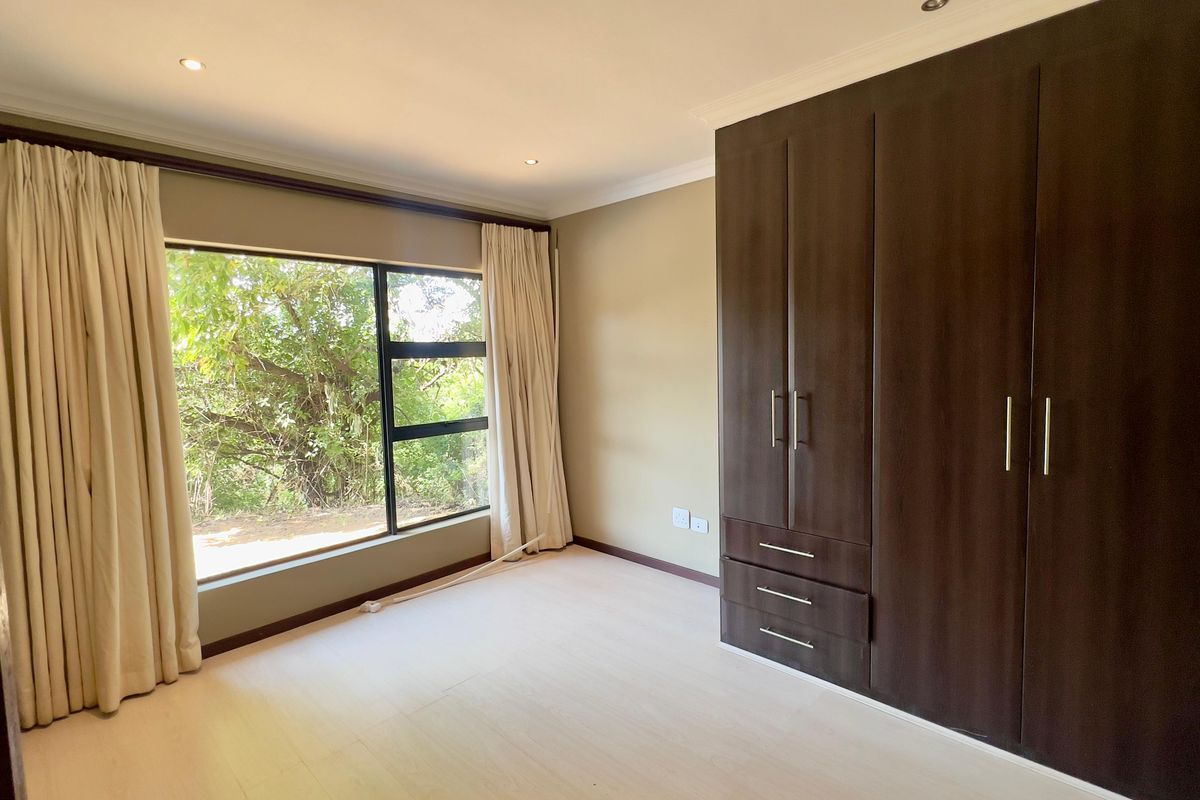 A bright and spacious bedroom featuring built-in dark wood cupboards, modern laminate flooring, and large windows with natural light.