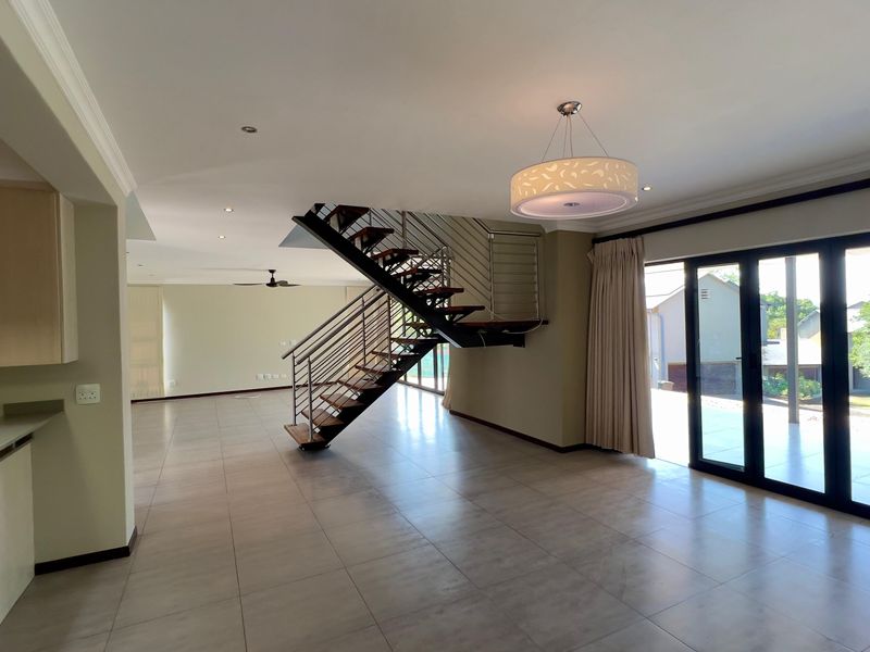 Spacious open-plan living area featuring modern tiled floors, a striking open-tread staircase with stainless steel balustrades, and large sliding doors leading to the outdoors.