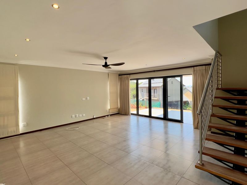 Spacious open-plan living area featuring large format floor tiles, recessed lighting, a ceiling fan, and a modern staircase with timber treads.