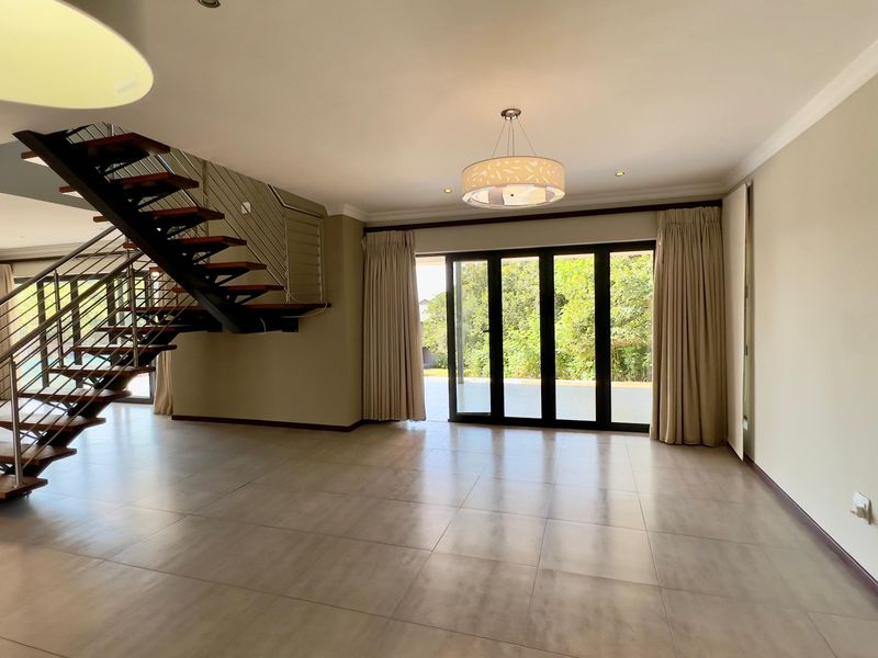 Spacious open-plan living area featuring a modern open-tread staircase with stainless steel balustrades, large format floor tiles, and sliding doors leading to the garden.