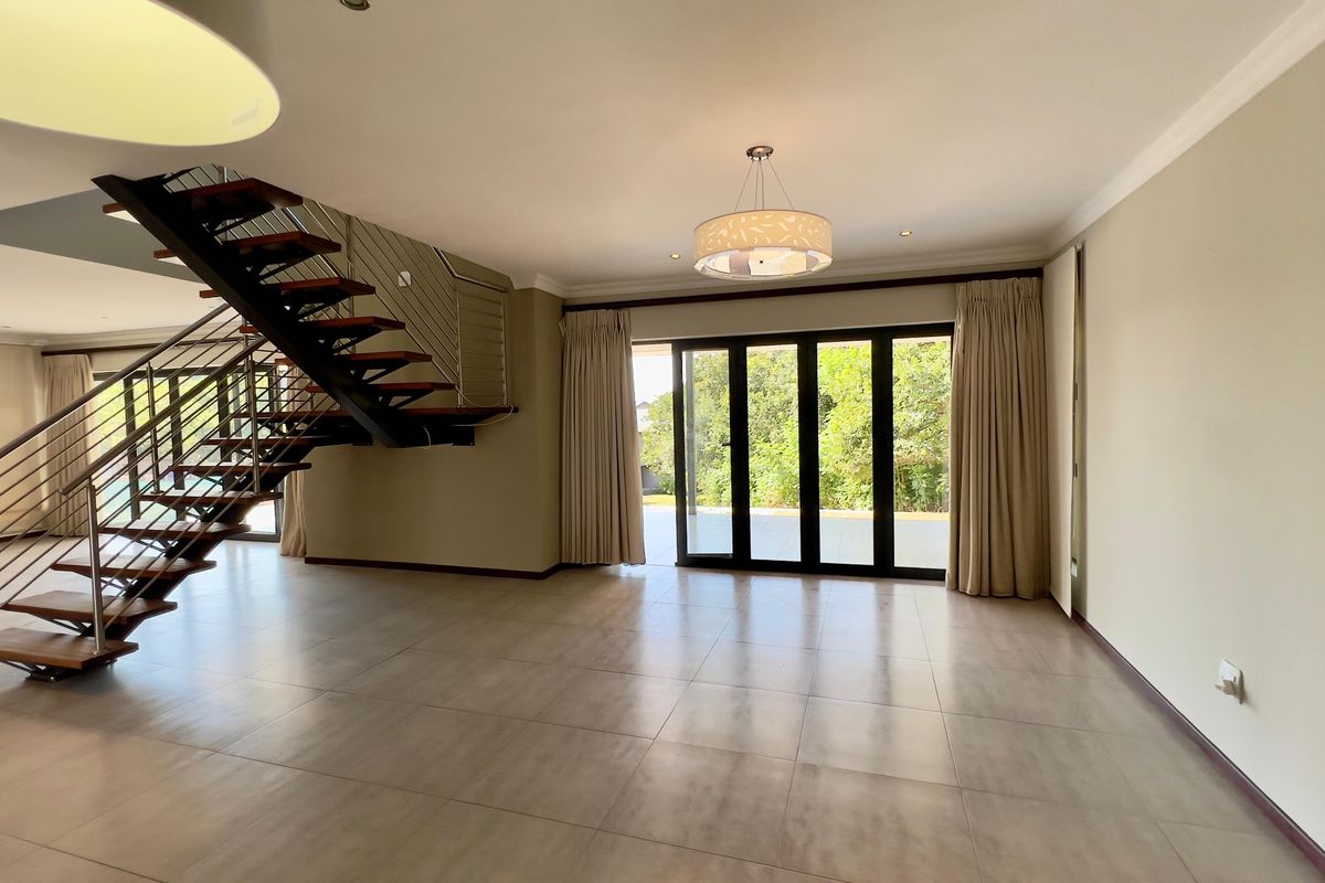Spacious open-plan living area featuring a modern open-tread staircase with stainless steel balustrades, large format floor tiles, and sliding doors leading to the garden.