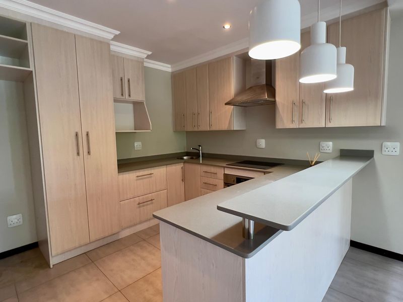 Modern kitchen featuring light wood cabinetry, stone countertops, a breakfast bar, and integrated appliances, finished with neutral tiled flooring.