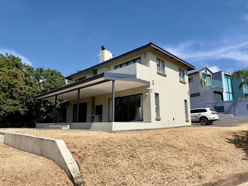 Rear view of a two-story house featuring a covered patio with a built-in braai, sliding glass doors, and a landscaped garden area.