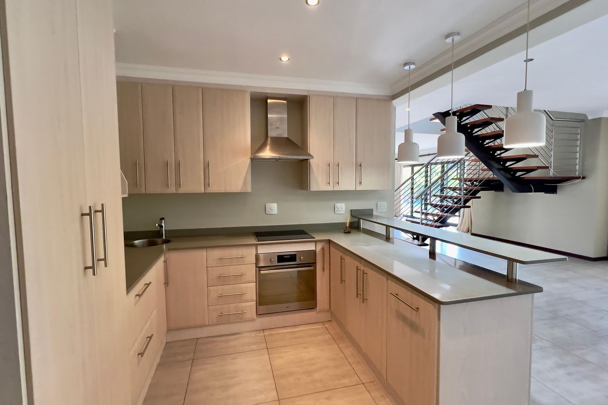 Modern kitchen featuring light wood cabinetry, stone countertops, integrated stainless steel appliances, and a breakfast bar overlooking the open-plan living area.