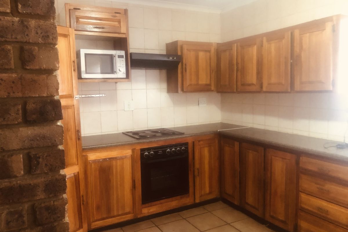 A functional kitchen featuring solid wood cabinetry, built-in oven, hob, extractor fan, and tiled flooring with a brick feature wall.
