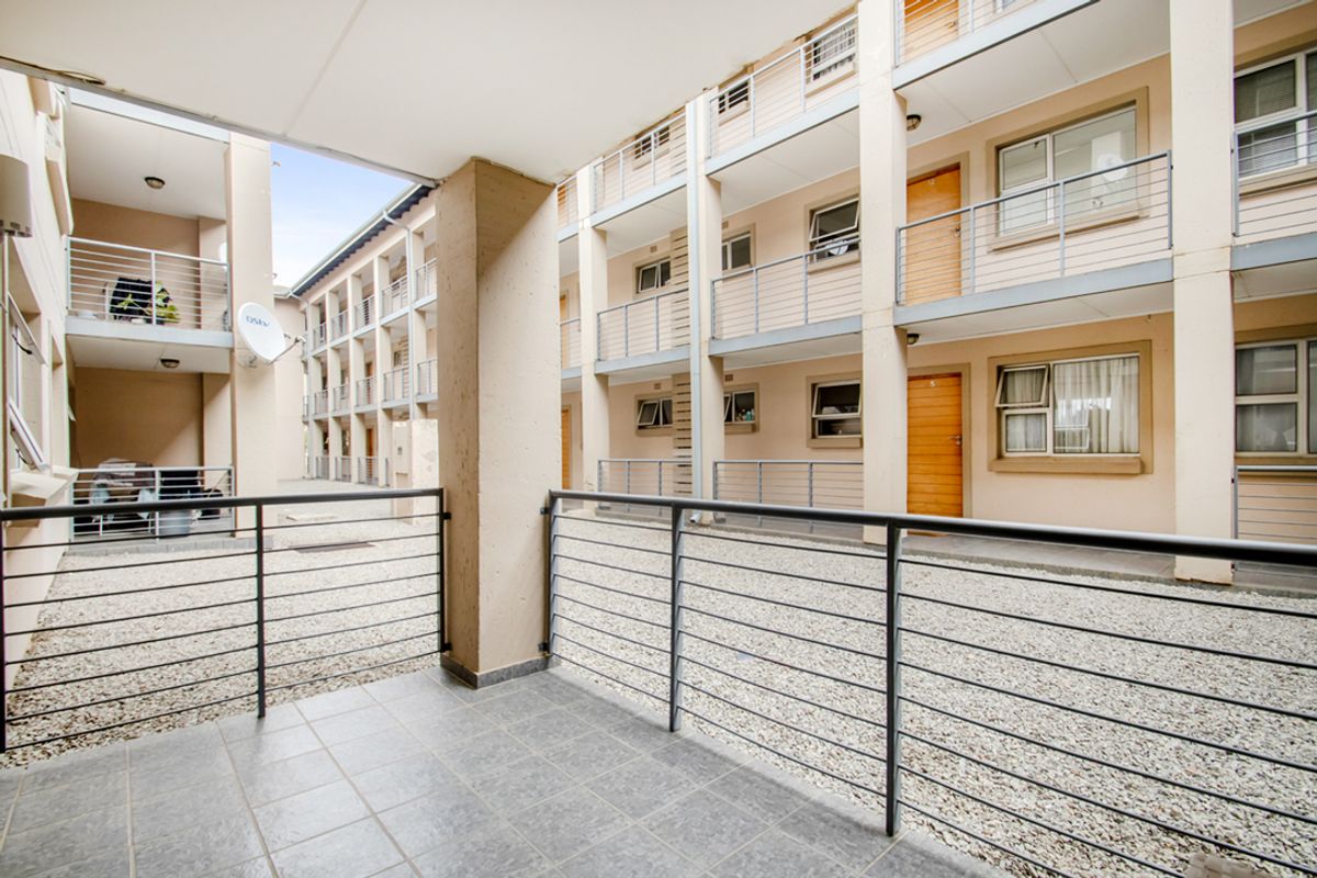 A view of the apartment complex courtyard featuring a tiled balcony, metal railings, and multi-level residential units with gravel ground cover.