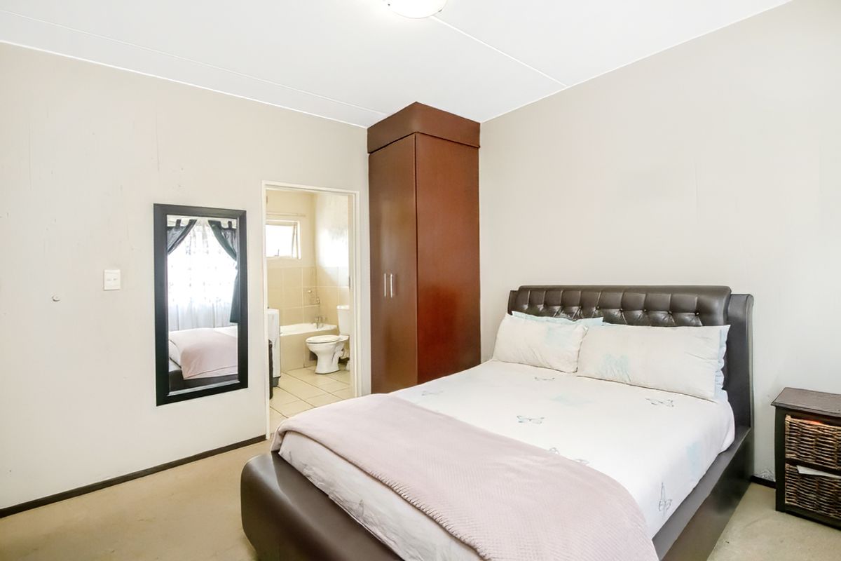 A bedroom featuring a built-in dark wood wardrobe and an en-suite bathroom with tiled flooring.