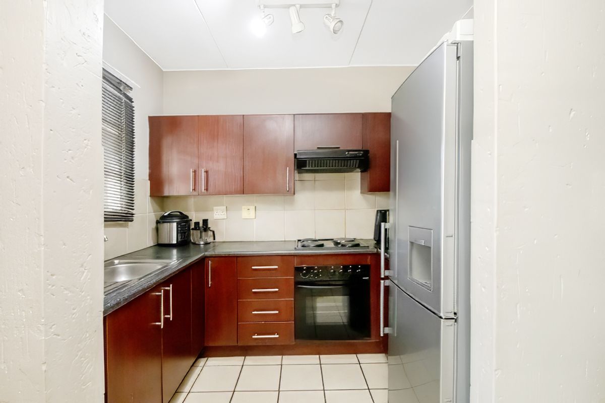Compact kitchen featuring dark wood cabinetry, tiled backsplash, built-in oven, hob, and extractor fan with tiled flooring.