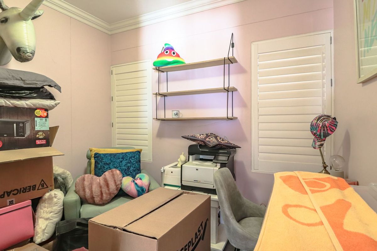 A bedroom featuring white plantation shutters and crown molding, currently utilized as a home office and storage space.