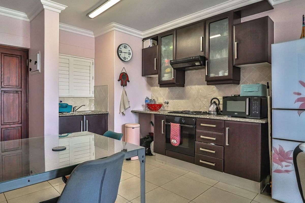 A functional kitchen featuring dark wood cabinetry, granite countertops, a built-in oven, hob, and extractor fan, with tiled flooring throughout.