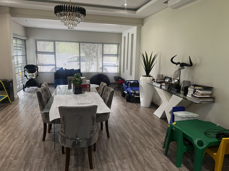 Spacious dining area featuring wood-look flooring, recessed ceiling lighting, a modern chandelier, and large windows with security shutters.
