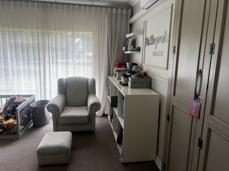 A bedroom featuring built-in cabinetry, wall paneling, and a large window with sheer curtains, providing a comfortable and well-lit living space.