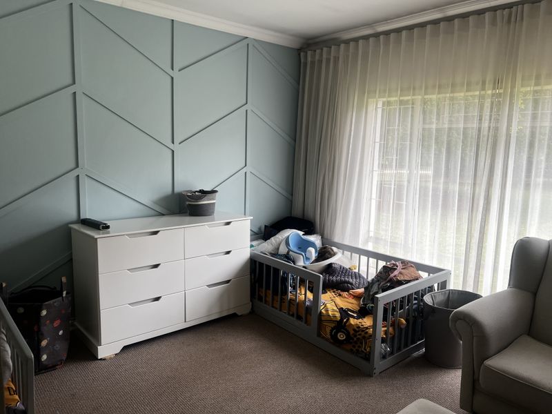A bedroom featuring a decorative chevron-patterned accent wall, neutral carpeting, and large windows dressed with floor-to-ceiling sheer curtains.