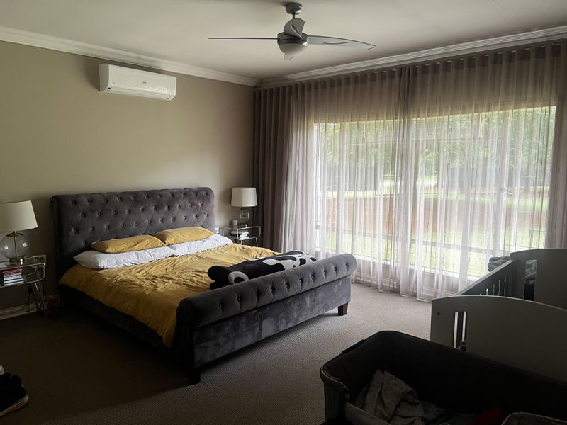 Spacious bedroom featuring a ceiling fan, wall-mounted air conditioning unit, and large floor-to-ceiling windows with elegant sheer curtains.