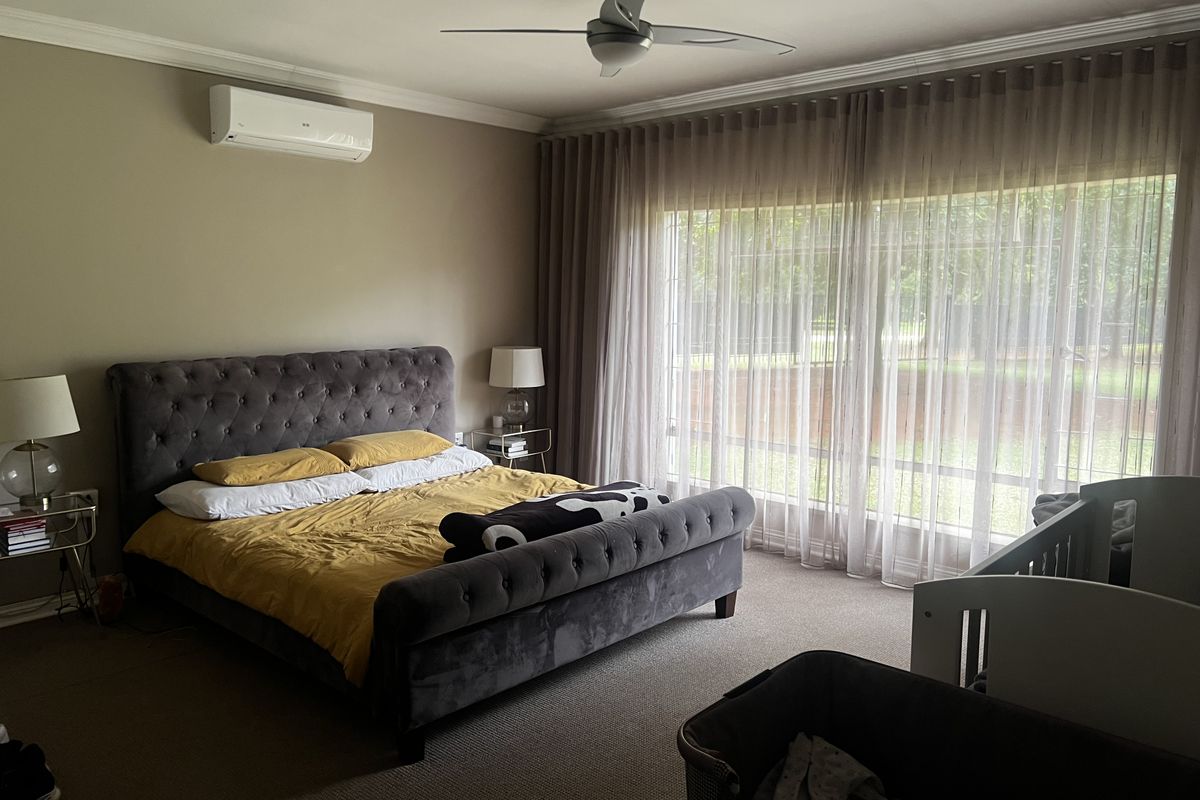 Spacious bedroom featuring a ceiling fan, wall-mounted air conditioning unit, and large floor-to-ceiling windows with elegant sheer curtains.