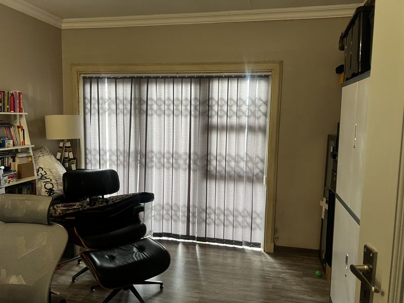 A functional room featuring laminate flooring, crown molding, and a large sliding door with vertical blinds providing access to the exterior.