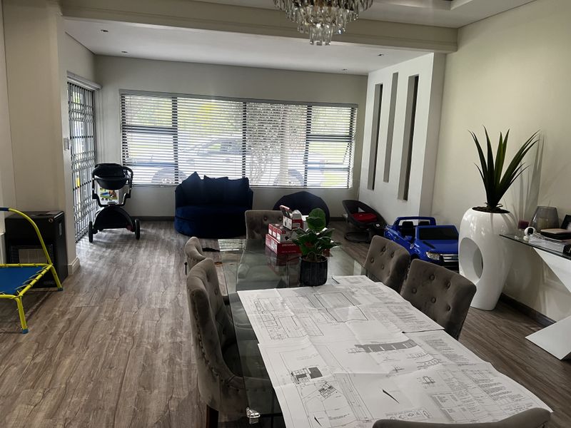 A bright dining area featuring wood-look flooring, recessed ceiling lighting, and large windows with horizontal blinds, offering a versatile space for family meals.