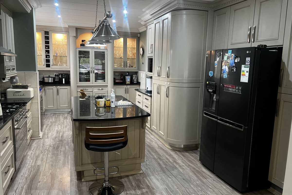 Spacious kitchen featuring custom cabinetry, a central island with a dark stone countertop, integrated lighting, and high-quality wood-look flooring.
