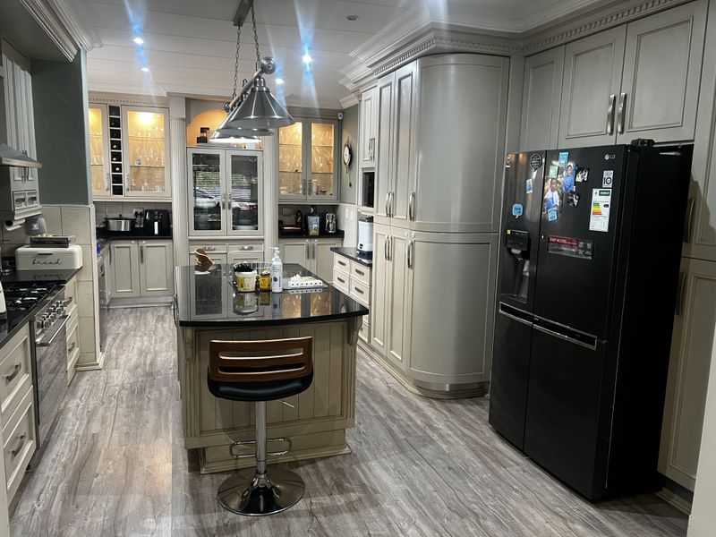 Spacious kitchen featuring custom cabinetry, a central island with a dark stone countertop, integrated lighting, and high-quality wood-look flooring.