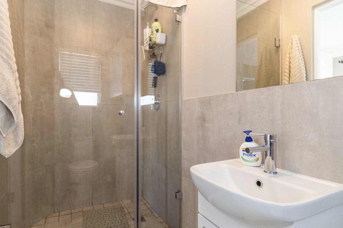 A modern bathroom featuring a glass-enclosed shower with neutral wall tiling and a white vanity basin with a chrome mixer tap.