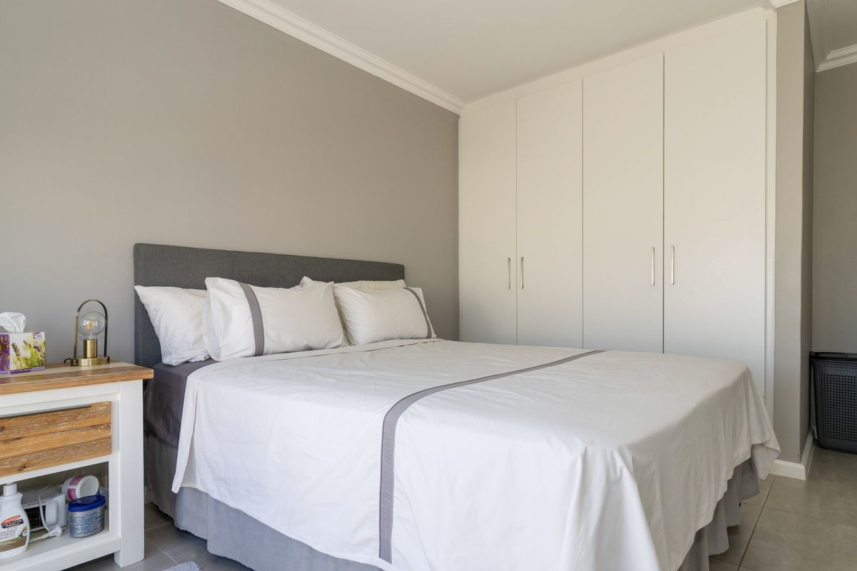 A well-maintained bedroom featuring neutral wall tones, tiled flooring, crown molding, and built-in floor-to-ceiling wardrobes.