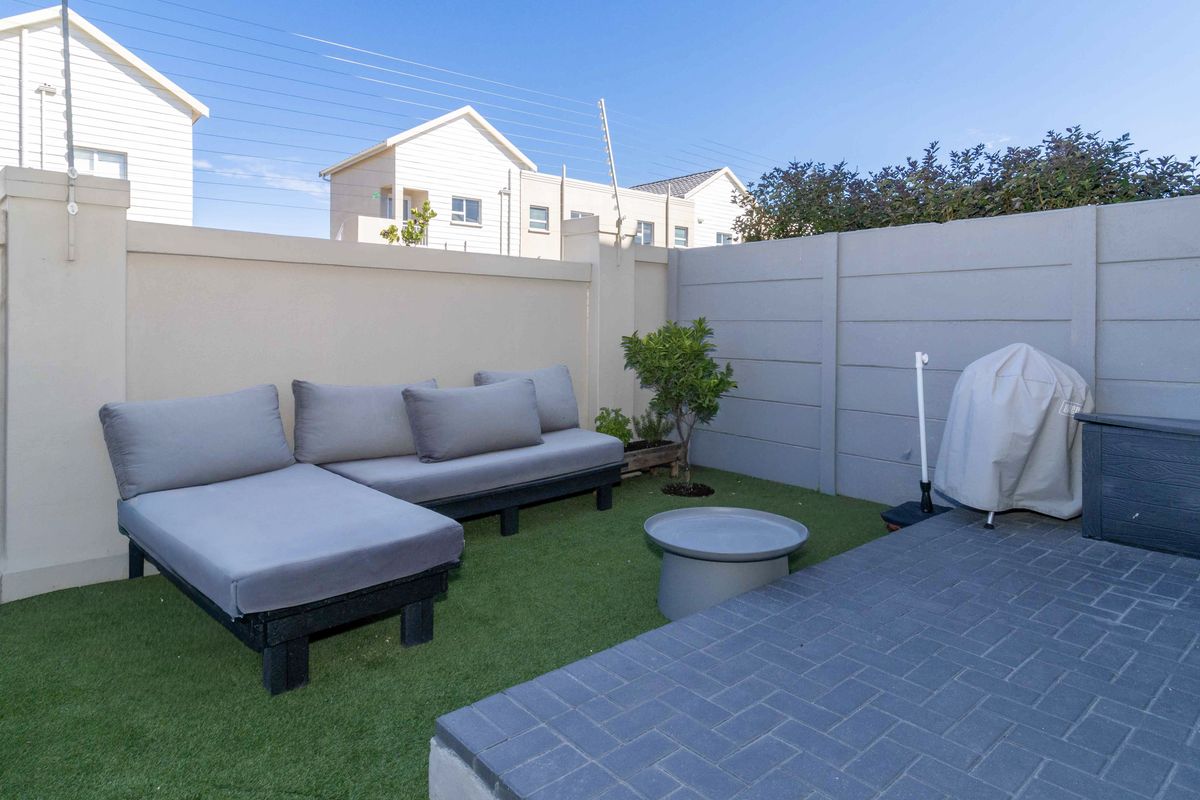 A private rear courtyard featuring a paved patio area and low-maintenance artificial lawn, enclosed by high boundary walls for added privacy.