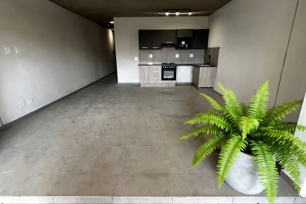 Open-plan living area featuring a modern kitchen with built-in cabinetry, oven, and hob, finished with neutral tiled flooring and exposed concrete-style ceiling.