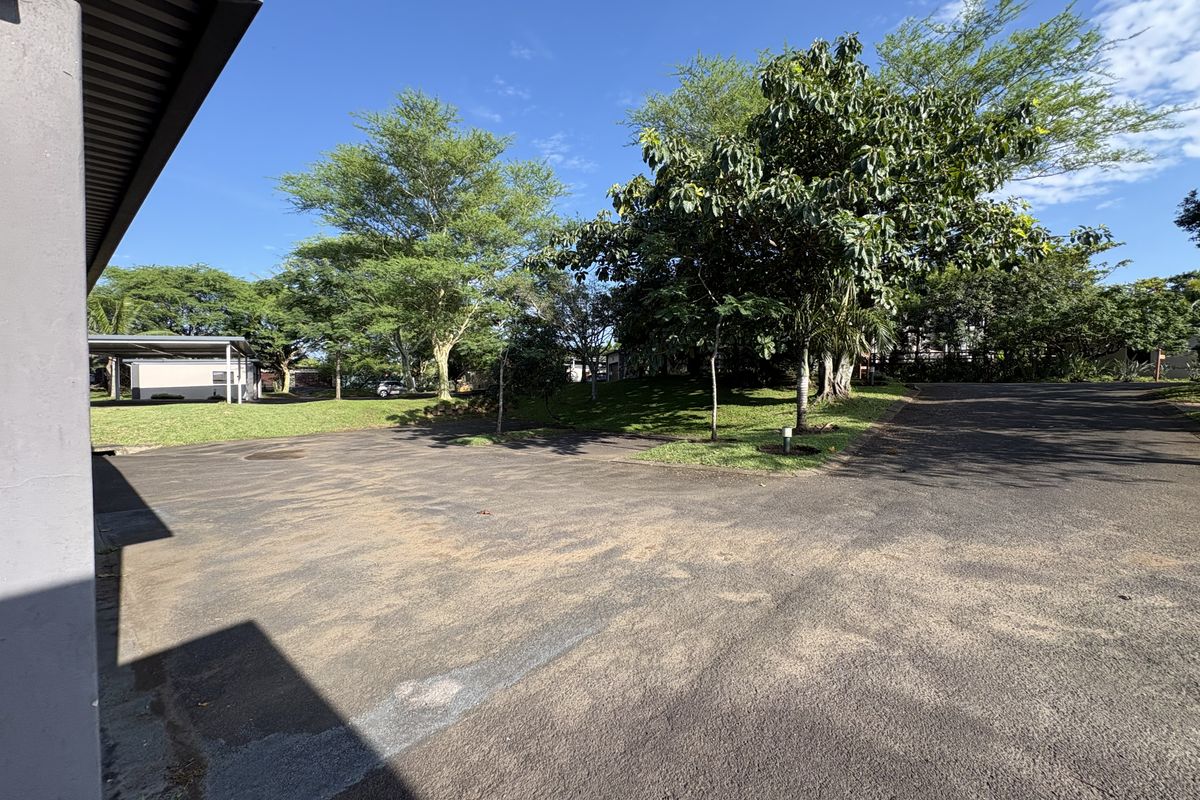 A view of the property's exterior driveway and surrounding landscaped garden area with mature trees.