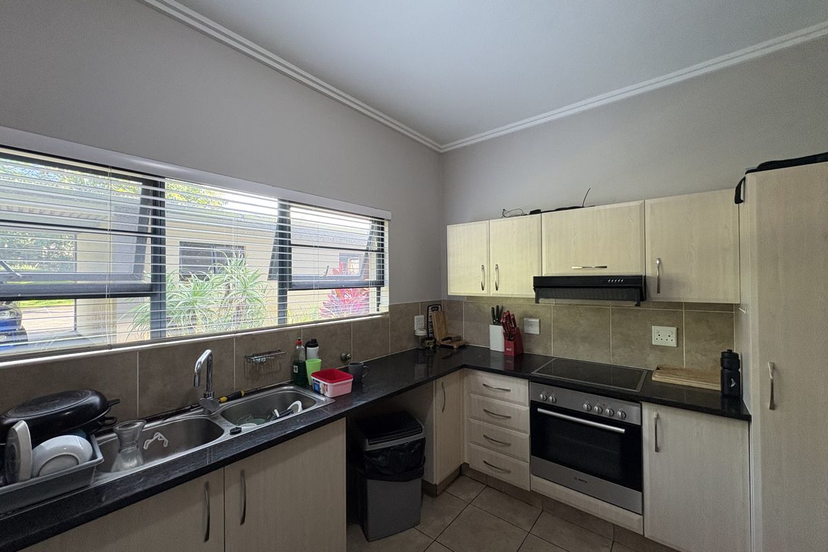 A functional kitchen featuring light-toned cabinetry, dark granite countertops, a built-in oven, hob, extractor fan, and a double-basin sink with tiled splashbacks.